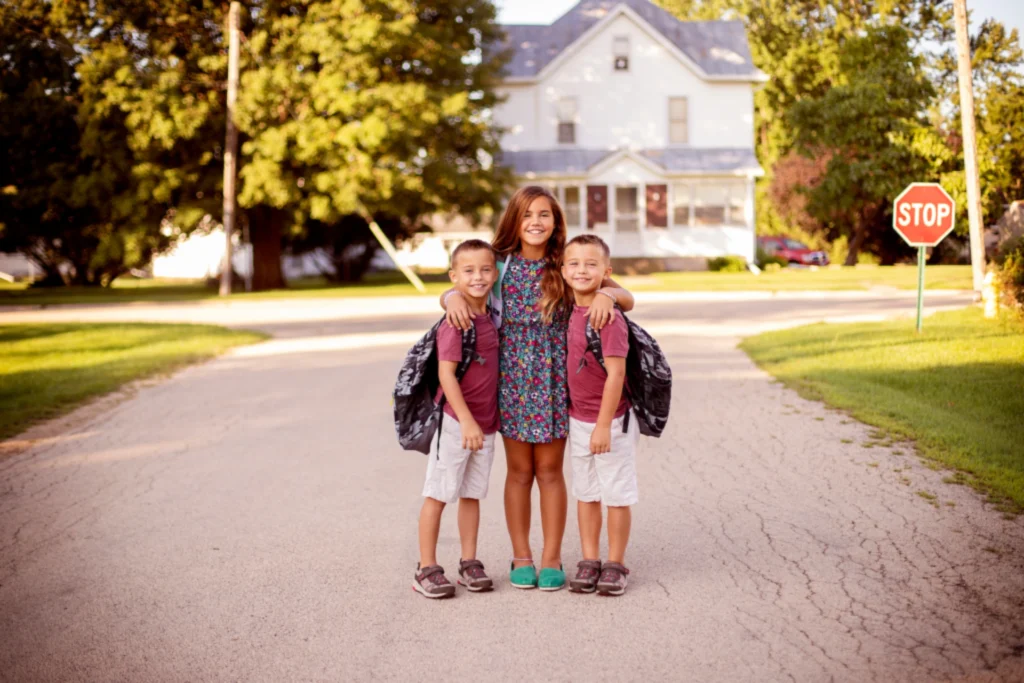 Sister with twin brothers standing on a road in front of a house