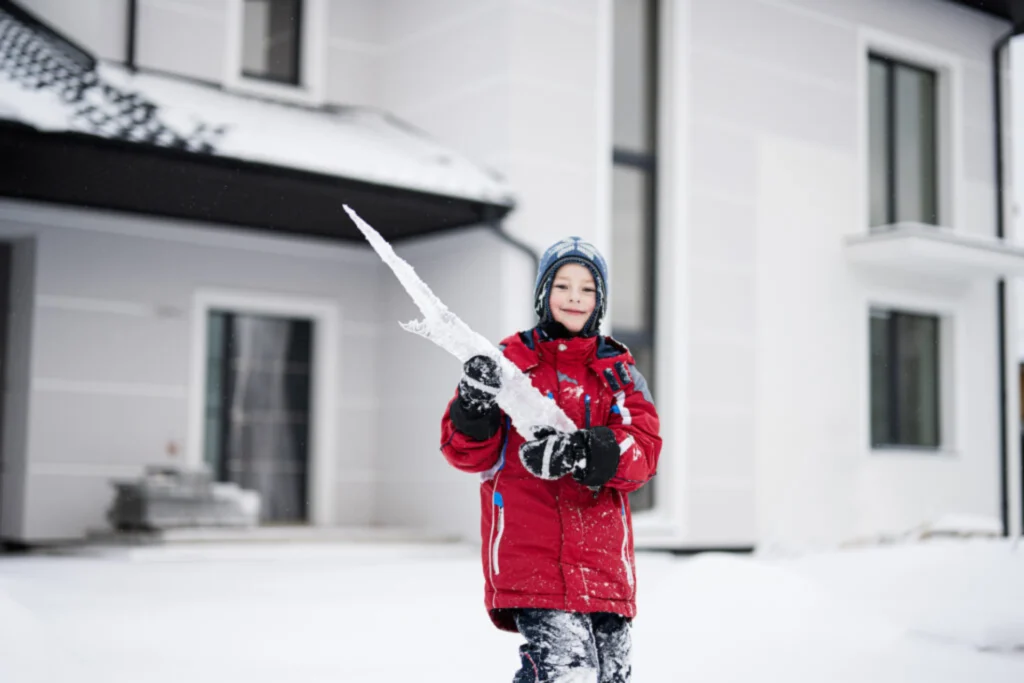 Young boy in red jacket holding a large ice icicle outdoors in winter
