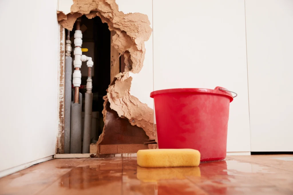 Plumbing repair scene with a broken dry wall exposing pipes and wet floor