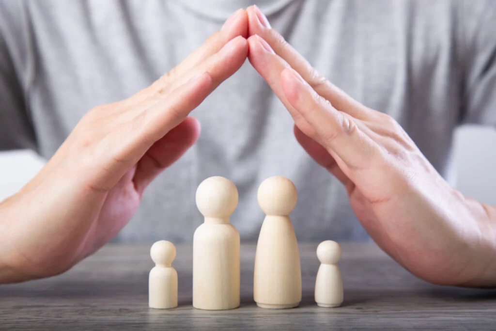Hands forming a protective roof over wooden figures representing a family