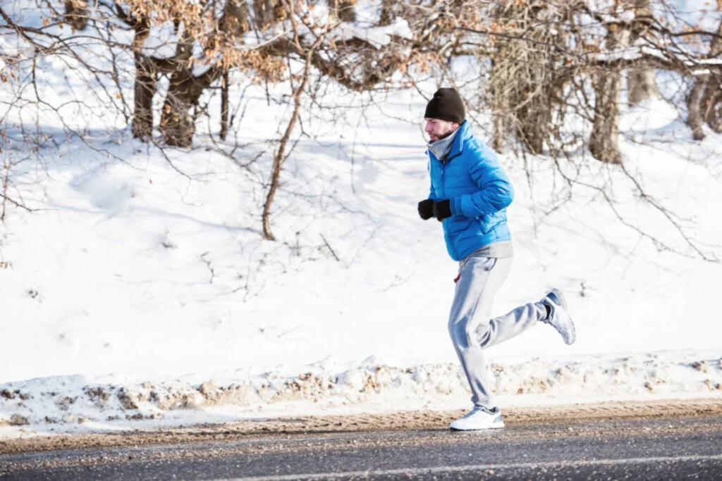 Man in blue jacket running on a snowy road during winter