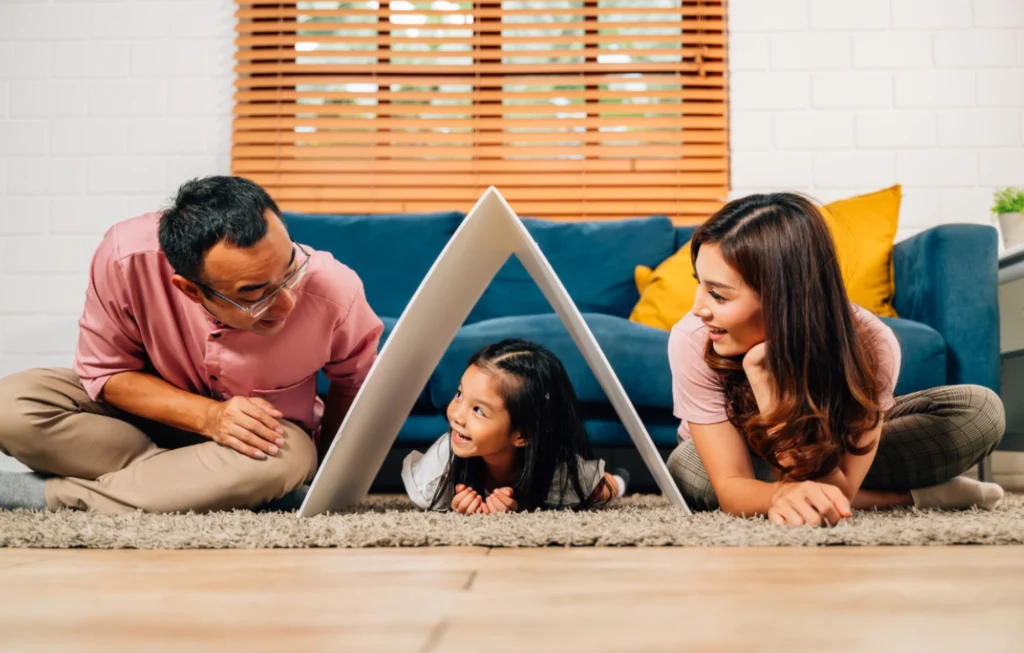Parents sitting on the floor holding a symbolic white roof over their daughter