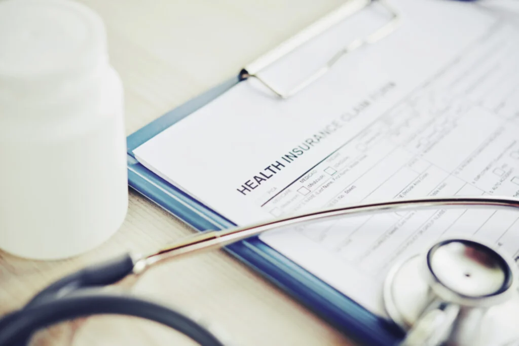 Medical insurance form with stethoscope and pill bottle on a desk