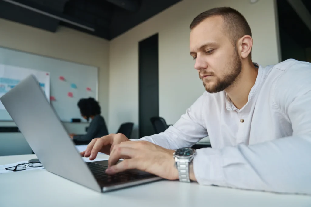 Young man in a white shirt typing on a laptop at his desk in a modern office