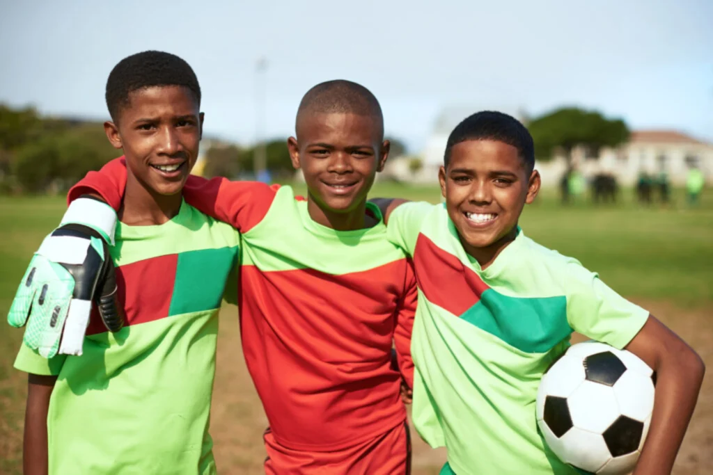 Three young boys in soccer uniforms smiling on a football pitch