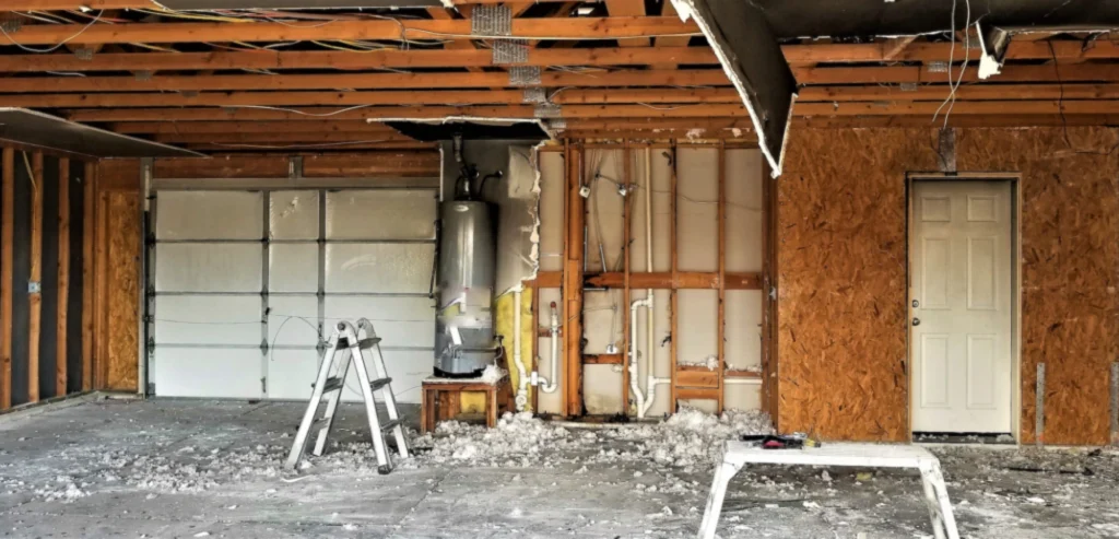 Damaged interior of a garage under restoration with exposed wooden framing and water heater