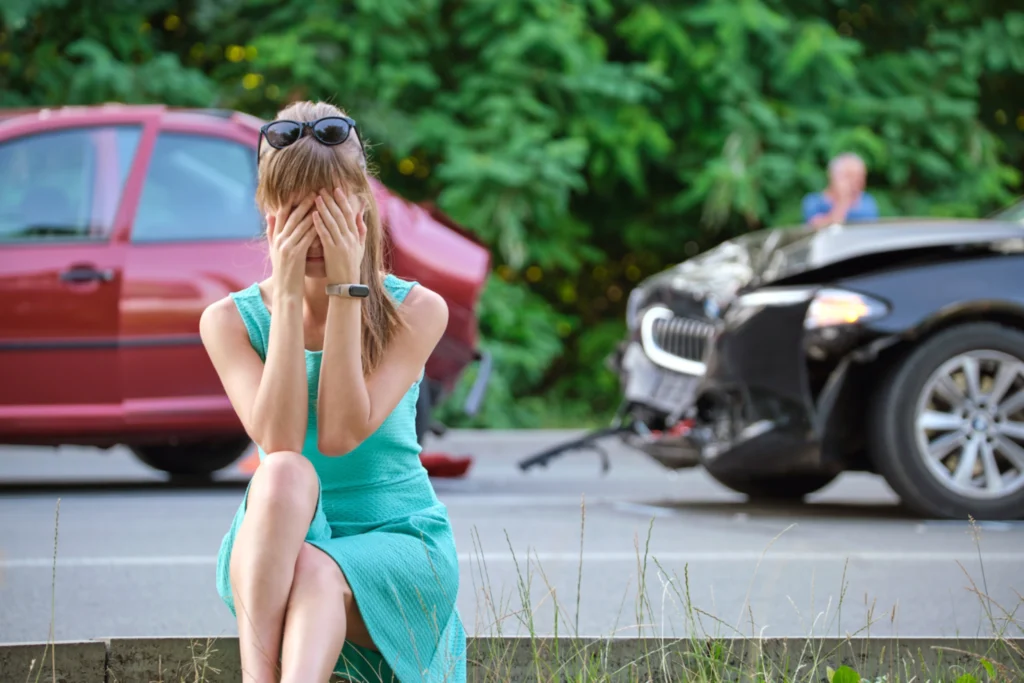 Stressed woman covering her face while sitting by the roadside after a car accident