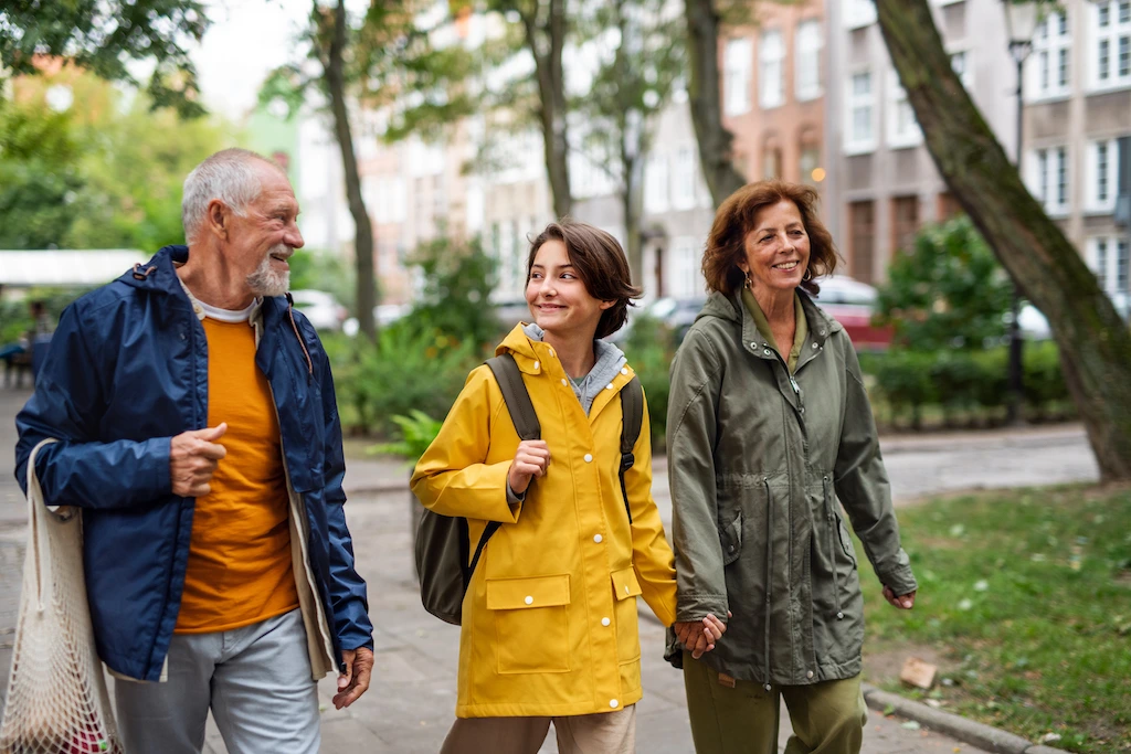 Older man, teenage girl, and middle-aged woman walking together in a green urban park.