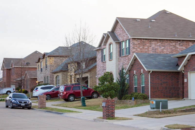 Brick houses in a residential neighborhood with driveways, parked cars, and front lawns.