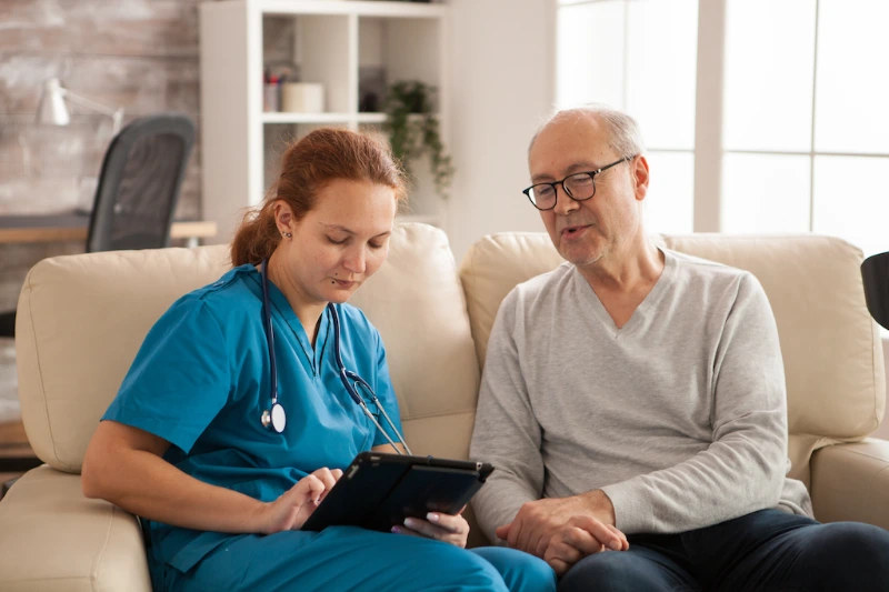 Healthcare nurse reviewing medical information with an elderly patient at home using a digital tablet.